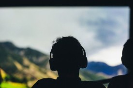 Man wearing headphones has shadowy figure painted against a mountain landscape.